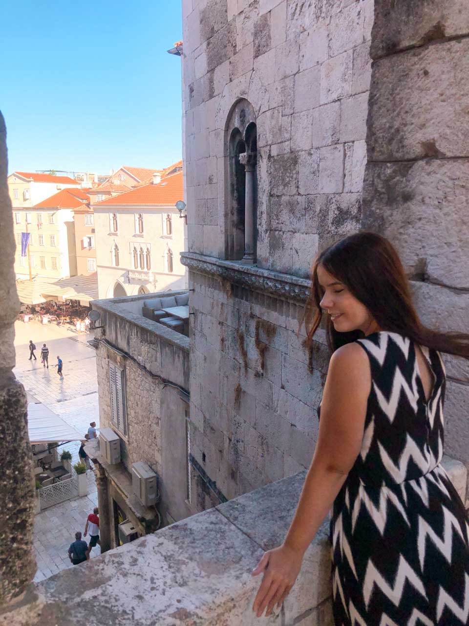 Girl in a black and white maxi dress standing on a terrace overlooking People's Square or Pjaca in Split Old Town