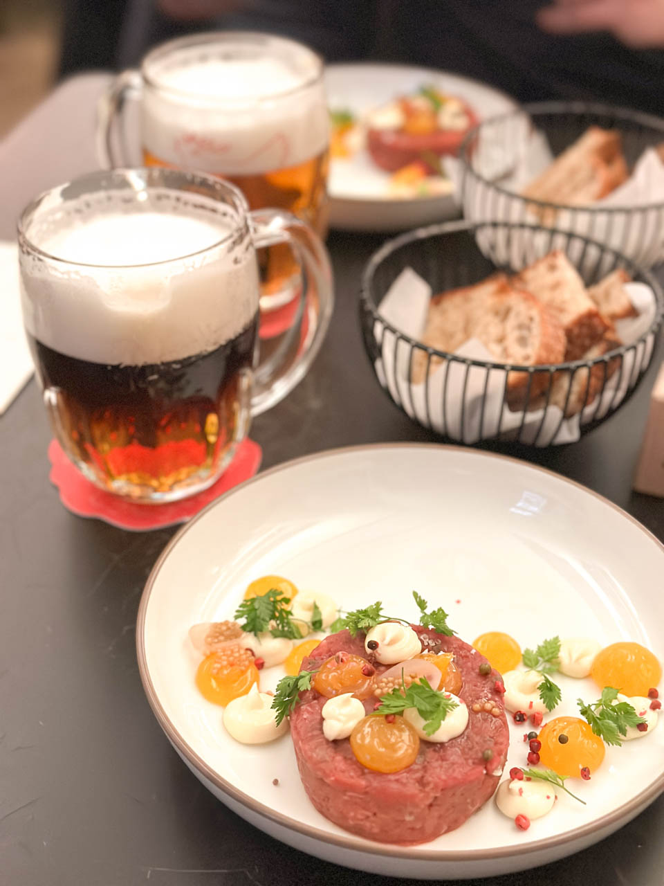 Two glasses of beer, two plates with beef tartare, and two bread baskets on a table at Červený Jelen in Prague