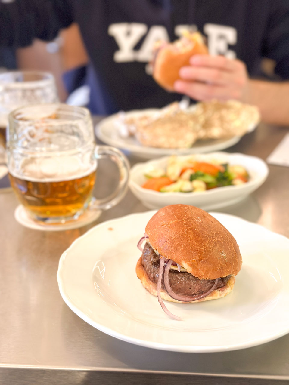 Two glasses of beer and two burgers with a side of steamed vegetables on a table at Kantýna in Prague
