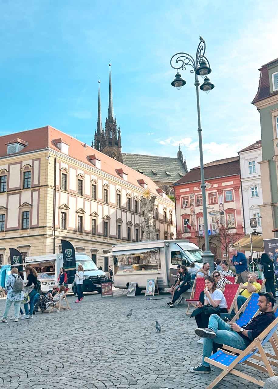 People lounging on chairs next to street food trucks on the Vegetable Market (Zelný Trh) in Brno, Czech Republic
