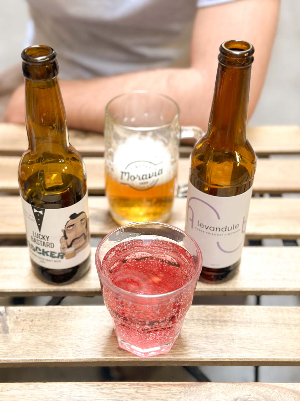 A bottle of craft beer, a bottle of lavender lemonade, and two glasses on a wooden table