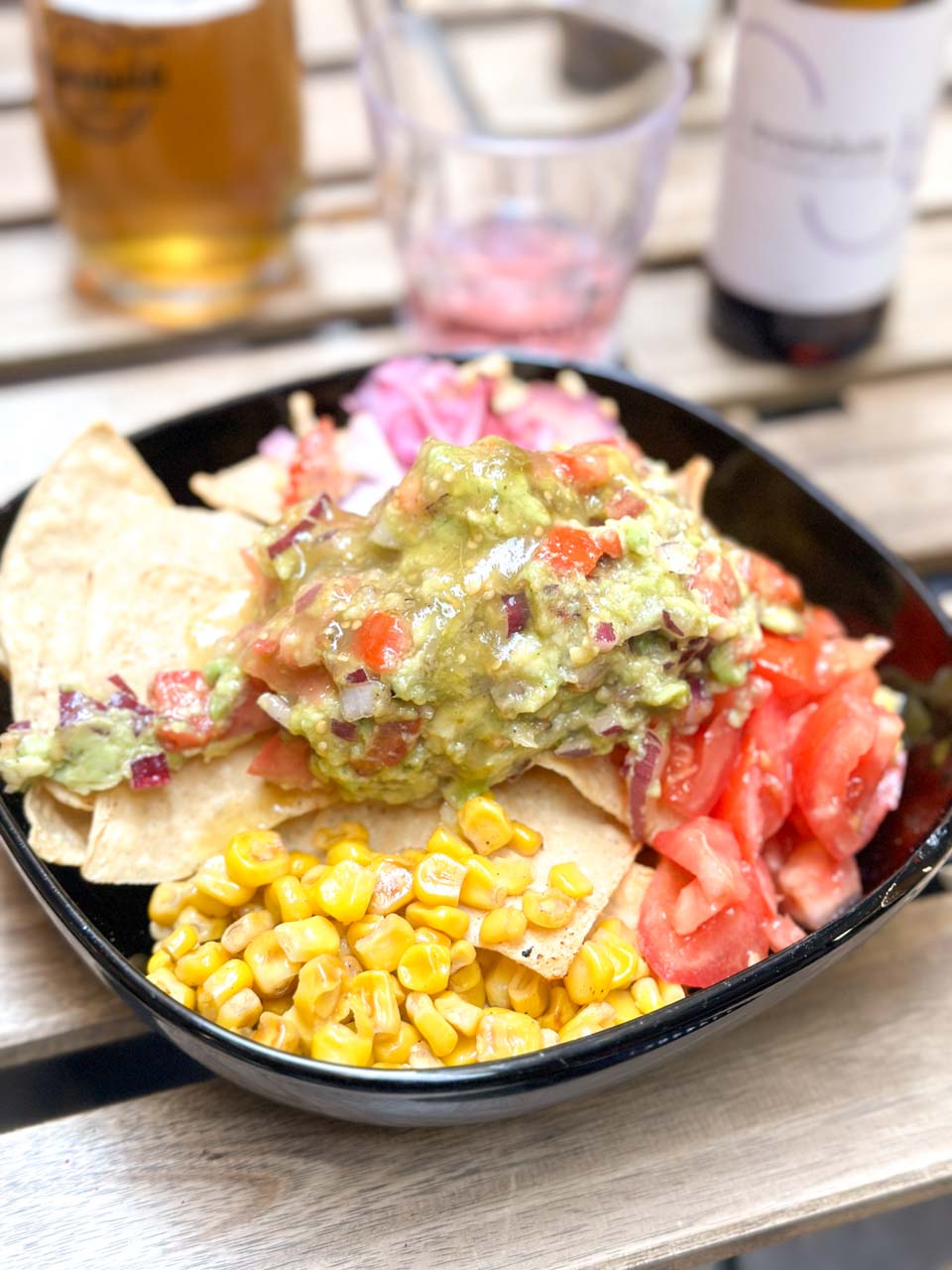 Appetising nachos platter, topped with guacamole, fresh tomatoes, and sweetcorn, served in a black bowl