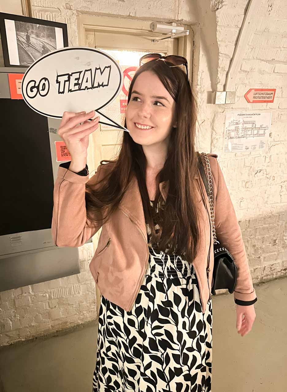 A woman holding a speech bubble sign that reads "GO TEAM" inside the 10-Z Bunker in Brno, Czech Republic