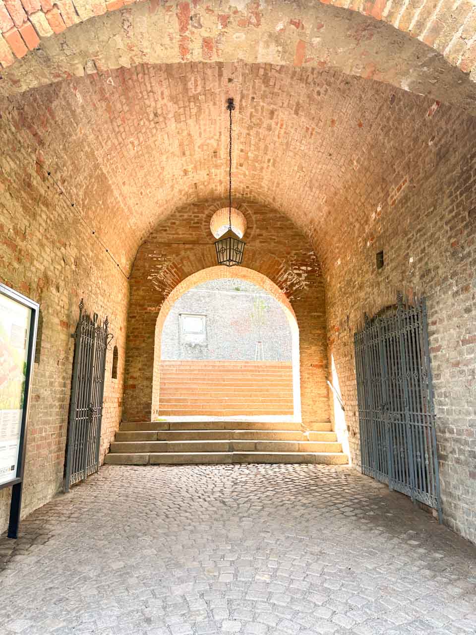 An old brick archway with iron gates and a hanging lantern in a courtyard leading to Špilberk Castle in Brno