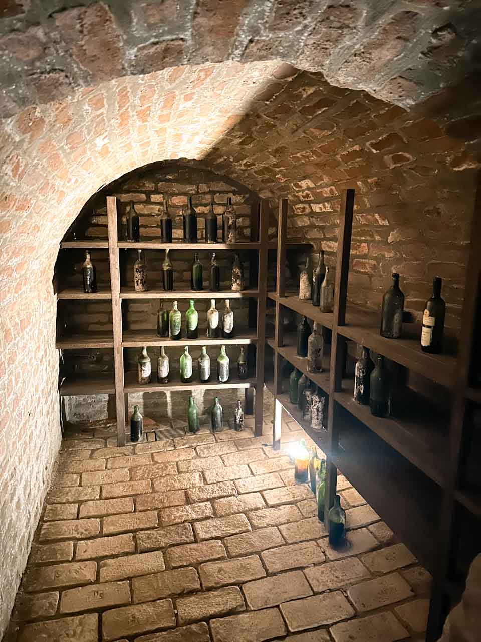 Brick wine cellar with vintage bottles on wooden shelves under an arch in the Labyrinth under the Vegetable Market in Brno, Czech Republic