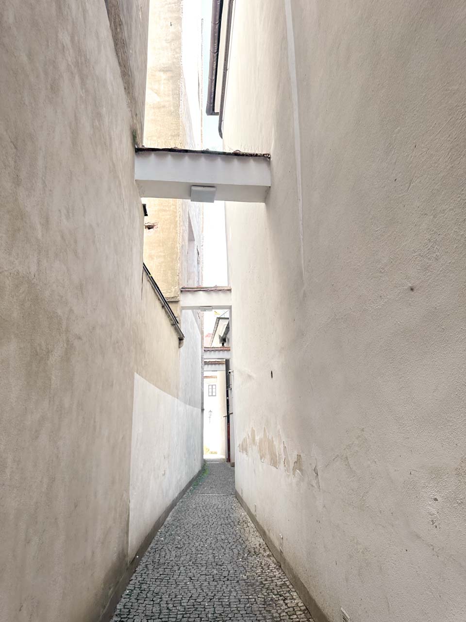 A narrow, cobbled alleyway lined by tall white walls in Brno, Czech Republic