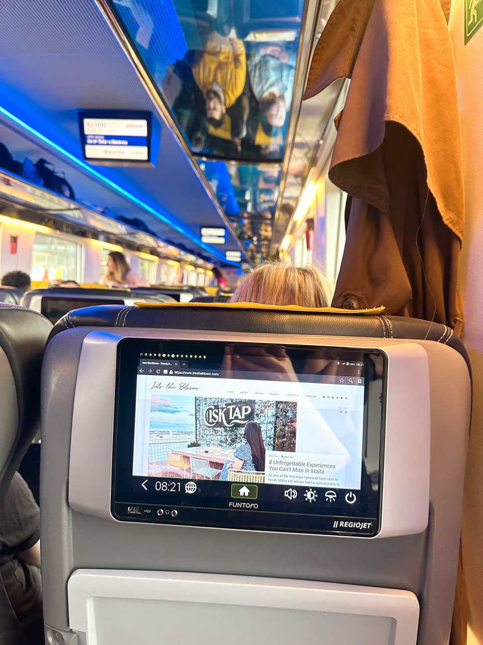 The interior of a RegioJet train with a seatback entertainment system displaying a website