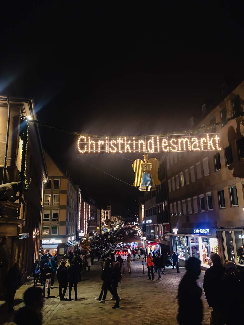 The iconic 'Christkindlesmarkt' sign lit up above a busy street at night, marking the entrance to the Nuremberg Christmas Market