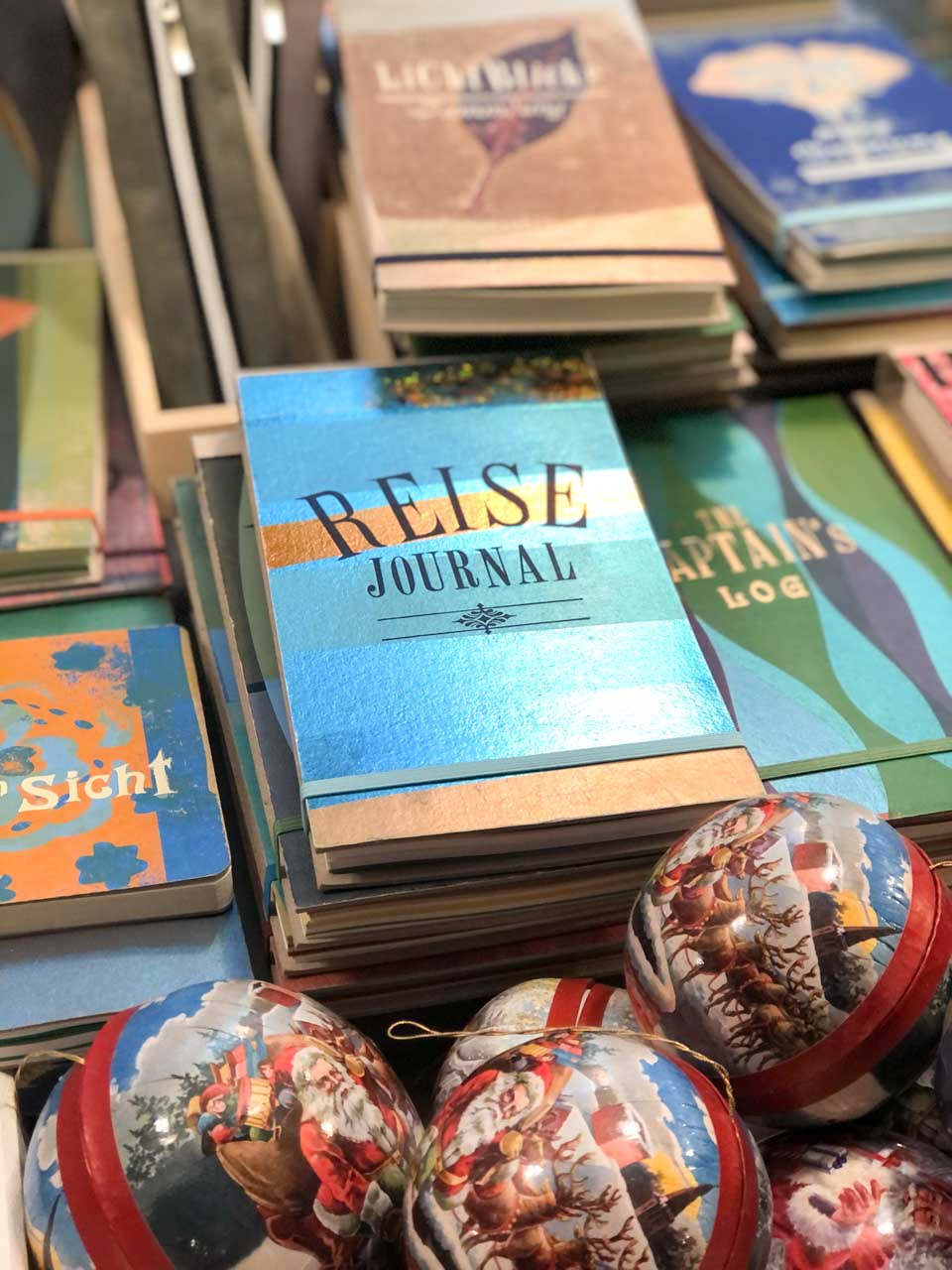 An assortment of travel journals with colourful covers next to decorative Christmas baubles on offer at the Nuremberg Christmas Market