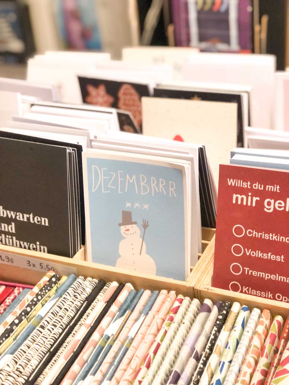 A display of greeting cards at the Christkindlesmarkt in Nuremberg, with one card featuring the word 'DEZEMBRRR' above a whimsical snowman illustration