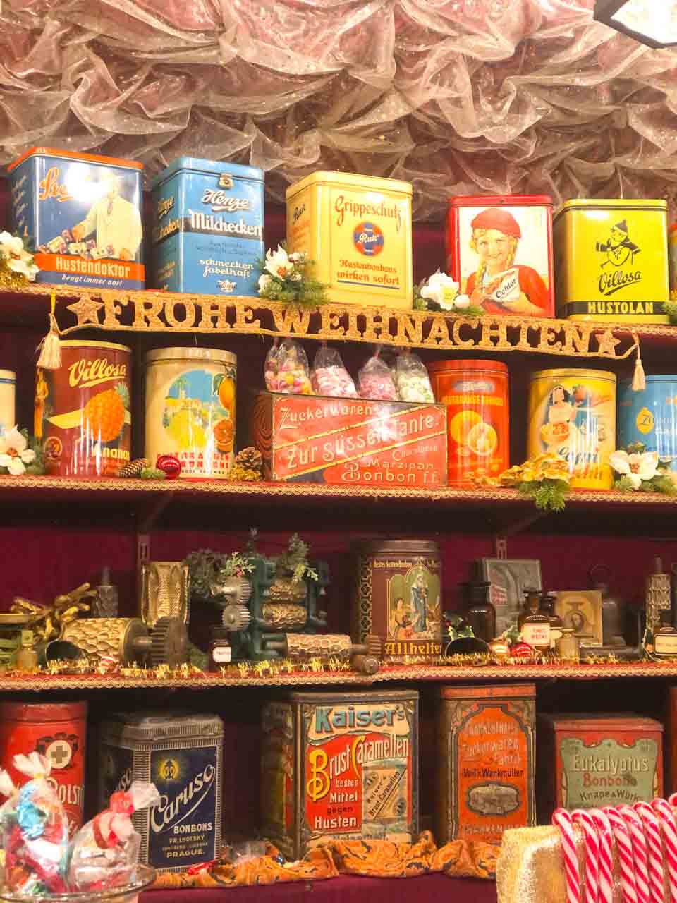 A vintage-themed stall displaying classic German cough and cold remedies in colourful retro packaging, with a sign wishing 'Frohe Weihnachten' (Merry Christmas) above, at the Nuremberg Christmas Market