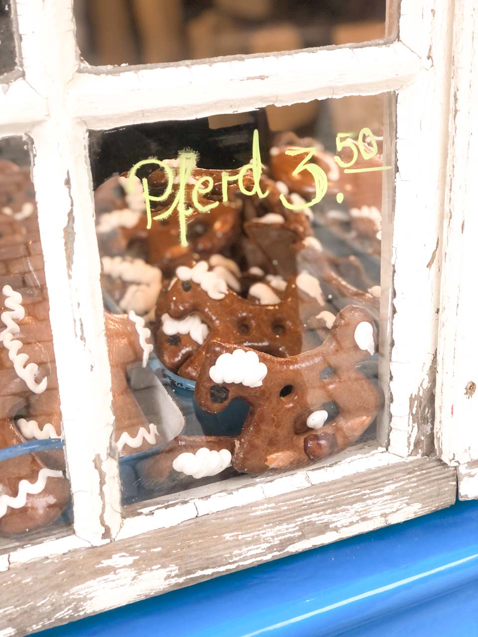 A close-up of a quaint shop window at the Nuremberg Christmas Market, displaying traditional gingerbread horses (Lebkuchen Pferd) with white icing