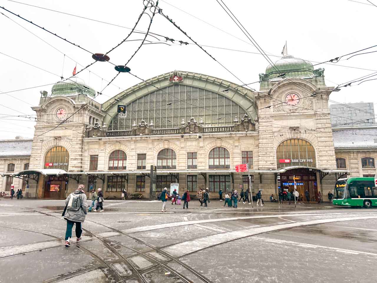 The main train station in Basel with people walking in front during a light snowfall