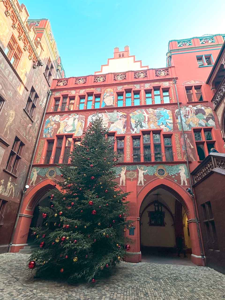 A decorated Christmas tree in the courtyard of Basel Town Hall, under a bright blue sky