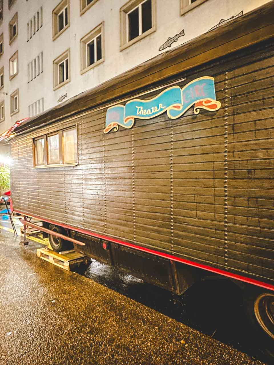 A vintage wooden trailer with 'Theater' sign, parked on the Rheingasse in Basel