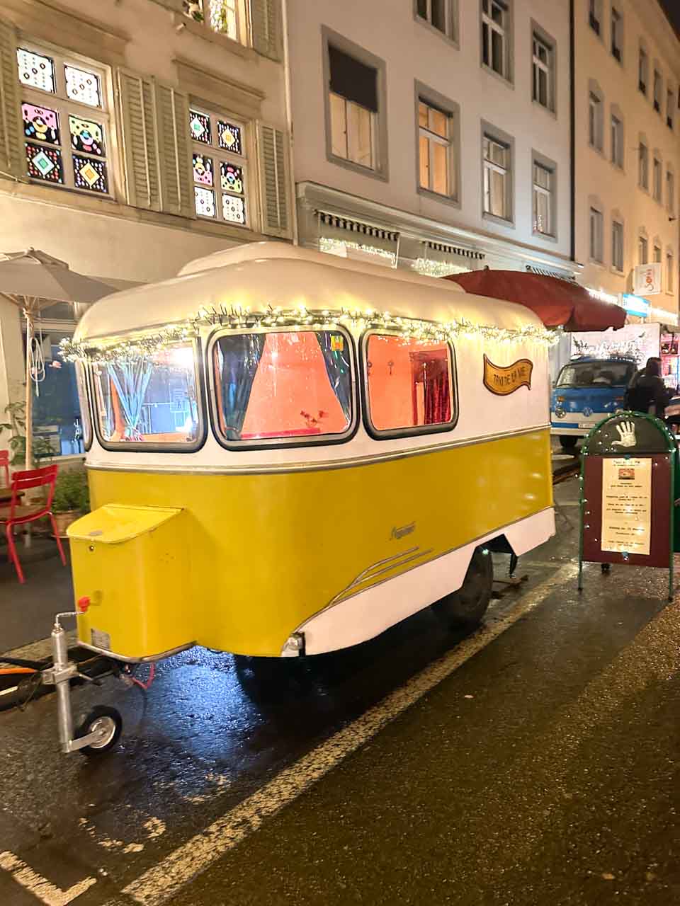 A vintage yellow trailer decorated with lights, serving as a food stall at the Adväntsgass im Glaibasel Christmas market in Basel