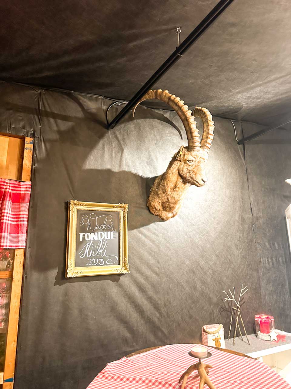 A majestic mountain goat's head mounted on the wall above a sign reading 'Wacker Fondue Stübli 2023'