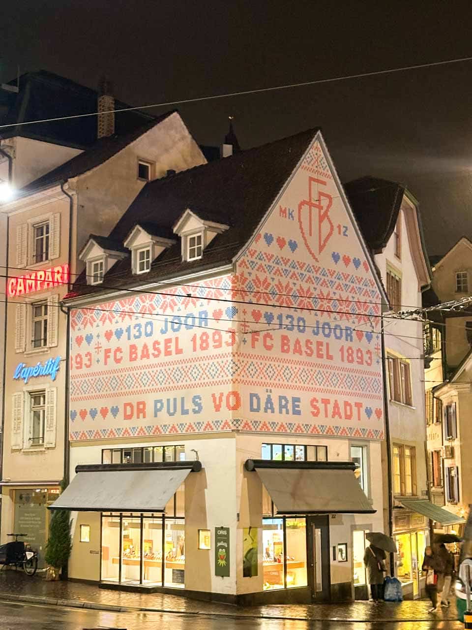 A building in Basel with '130 Years FC Basel 1893' written on its decorative facade, lit by street lights on a rainy night