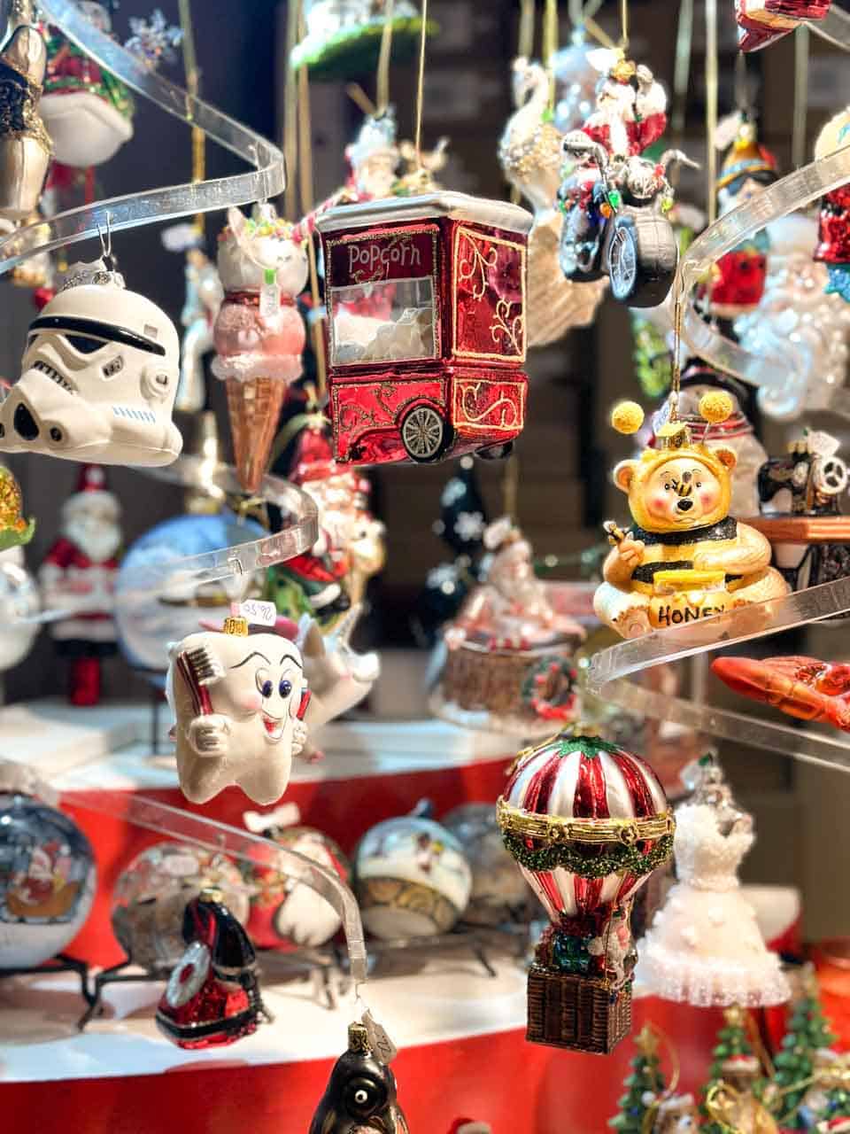 Various Christmas-themed tree ornaments on display, including a popcorn cart and a honey pot, at the Basel Christmas market on Barfüsserplatz