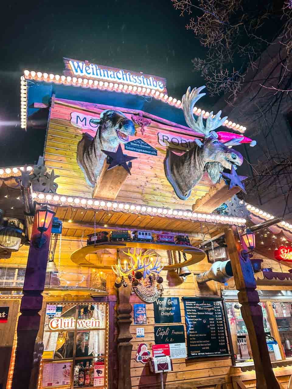 The 'Weihnachtsstube' wooden stall at Basel Christmas market, topped with two large moose heads and adorned with festive lights