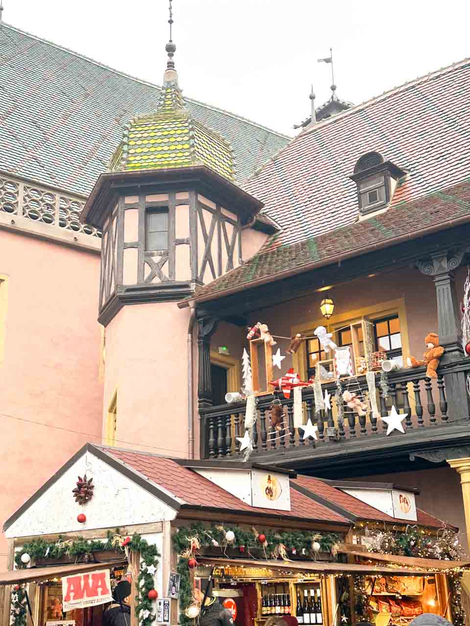The Koïfhus building in Colmar, providing a picturesque backdrop to a Christmas market stall decked out in festive garlands and decorations