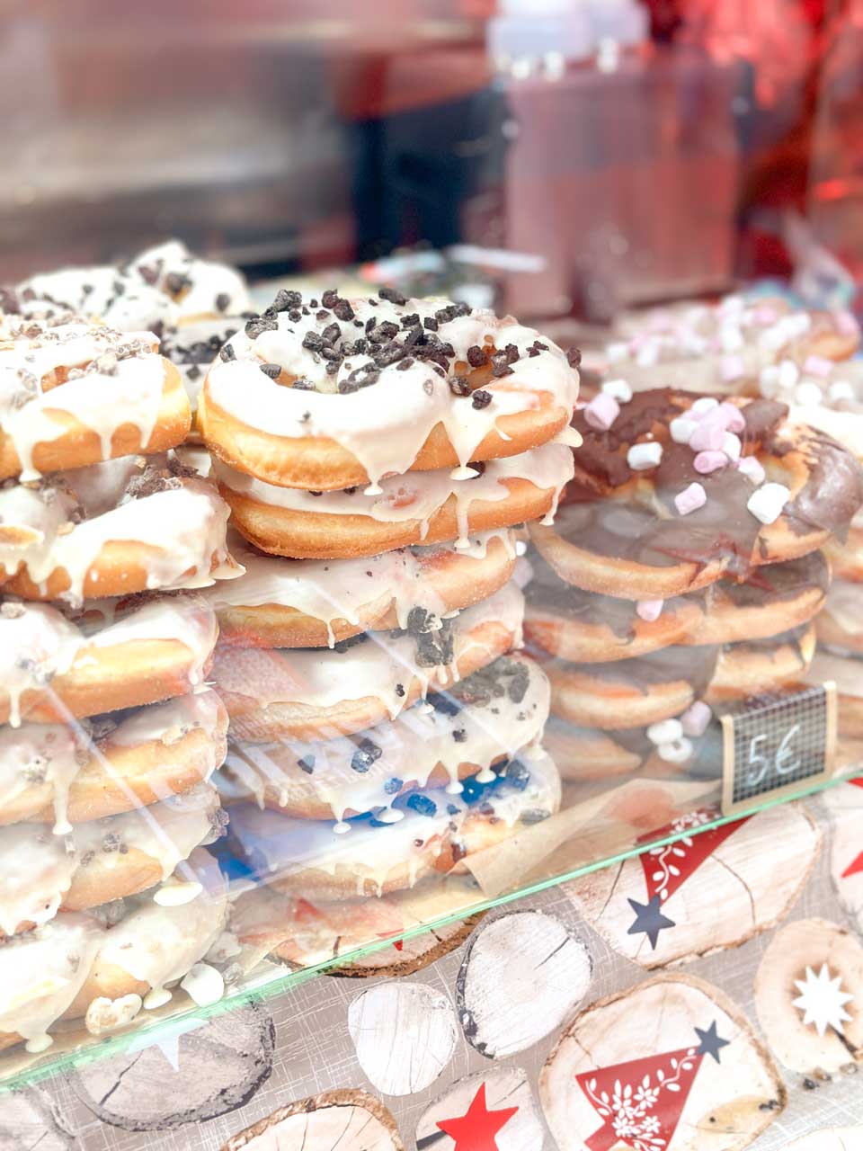 A display of glazed pretzel-shaped donuts with various toppings, including chocolate sprinkles and mini marshmallows at a Christmas market in Colmar
