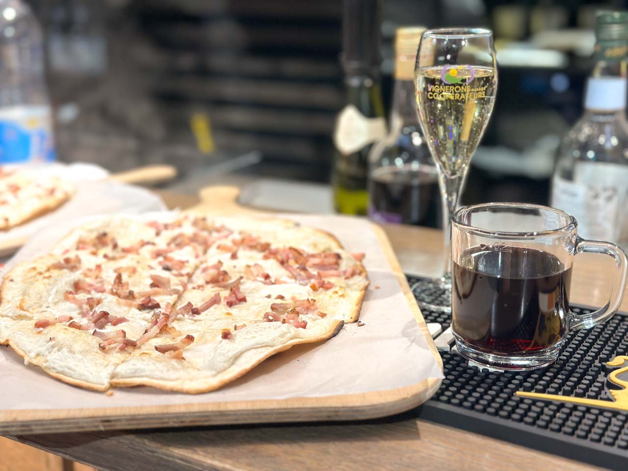 An Alsatian tarte flambée with diced bacon on top, next to a glass of Cremant D'Alsace wine and a cup of mulled wine