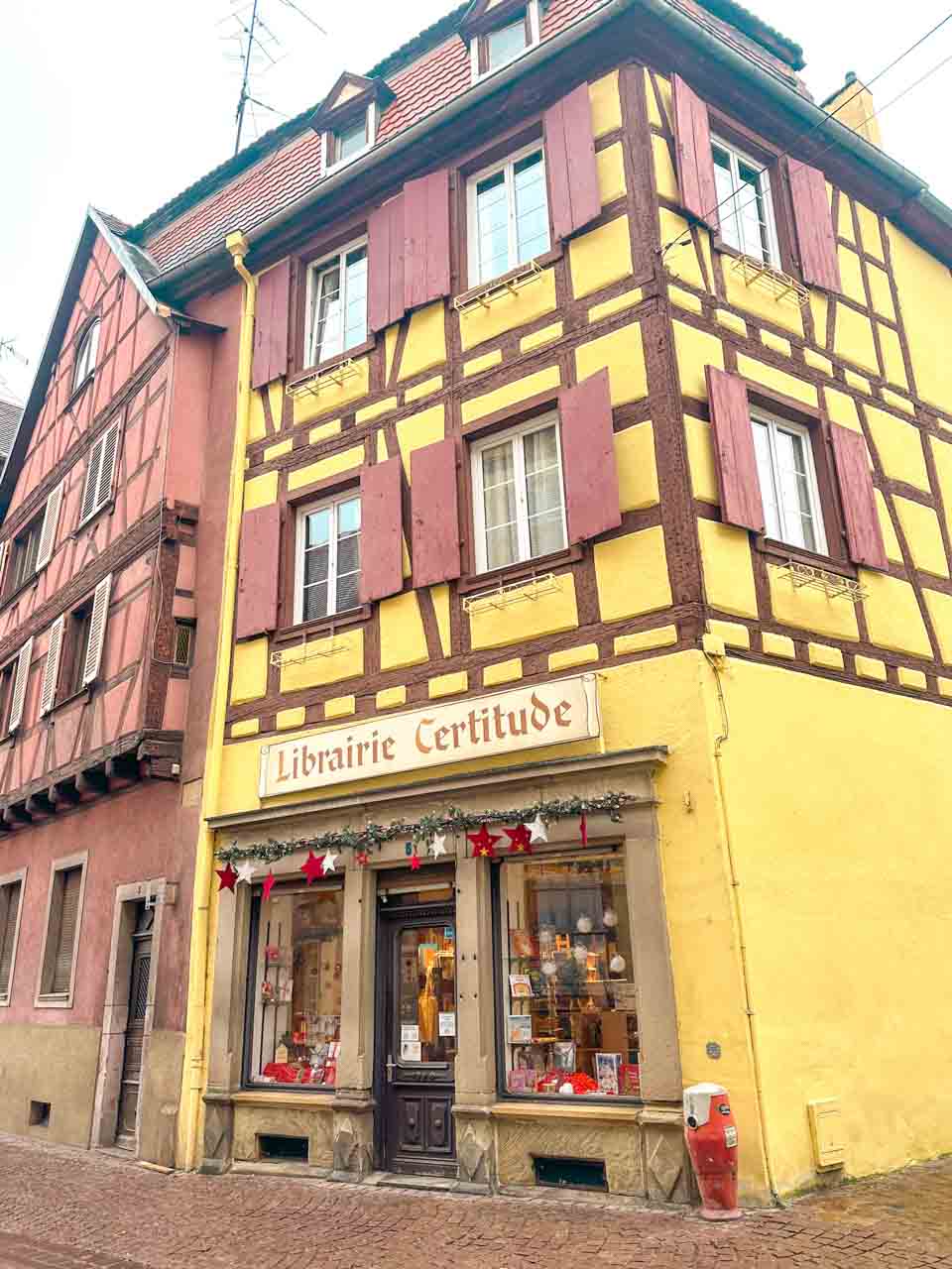A corner bookstore in Colmar with yellow walls and red window shutters