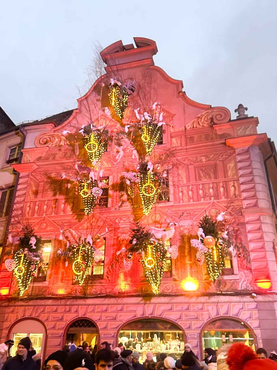 A striking facade of a building in Strasbourg illuminated with warm pink lighting and vibrant Christmas decorations