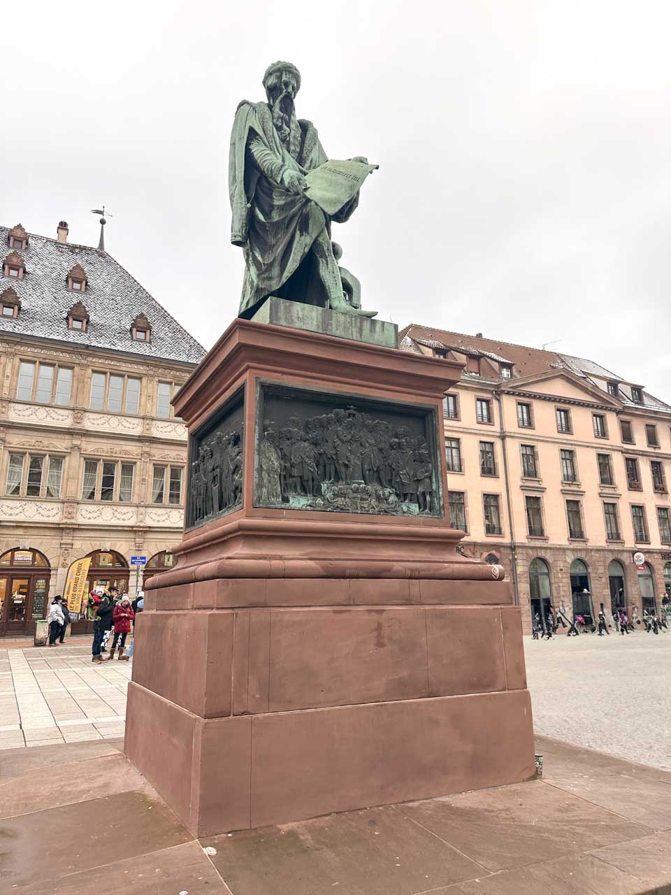 A bronze statue of Johannes Gutenberg with a book, standing tall on a pedestal on Rue Gutenberg in Strasbourg