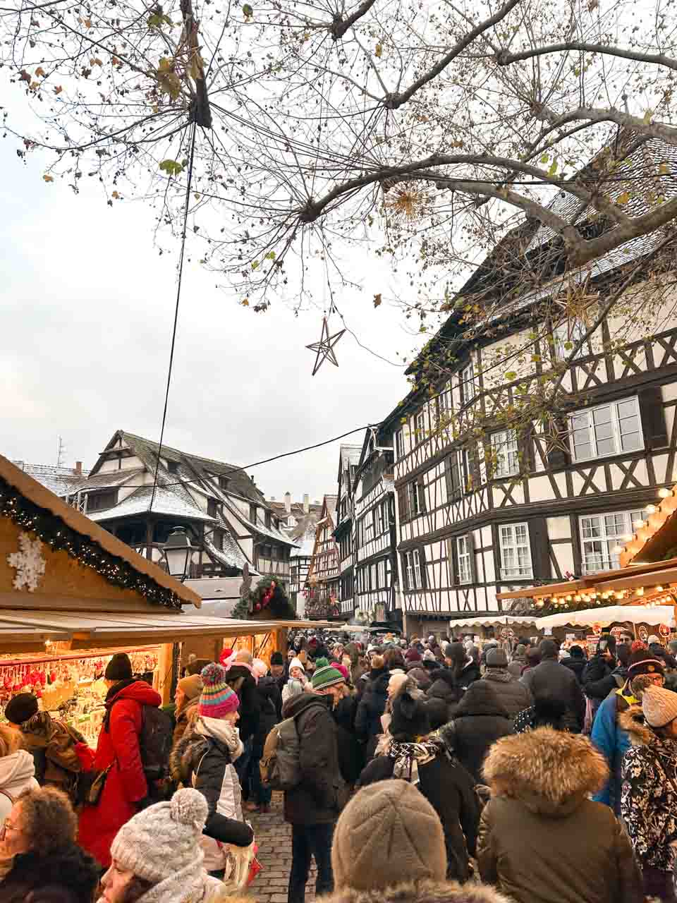 A bustling Christmas market scene in Strasbourg, with crowds of people shopping and enjoying the ambiance in front of historic half-timbered houses