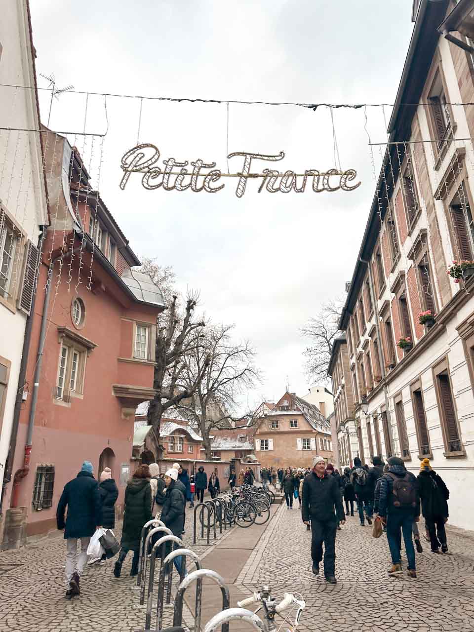 People strolling under a sign that reads "Petite France," surrounded by traditional architecture in Strasbourg