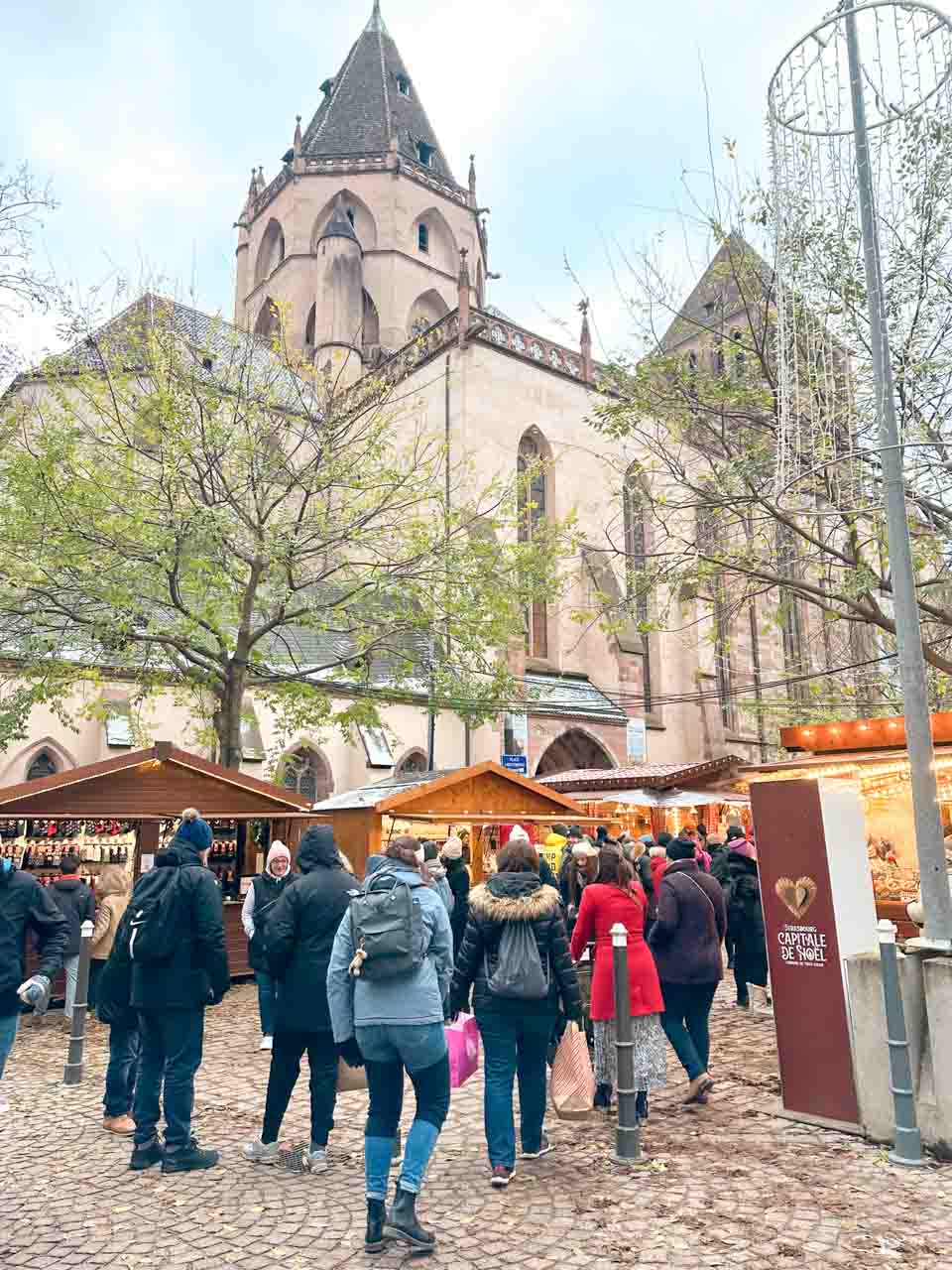 Shoppers walking past traditional market stalls near St. Thomas Church in Strasbourg