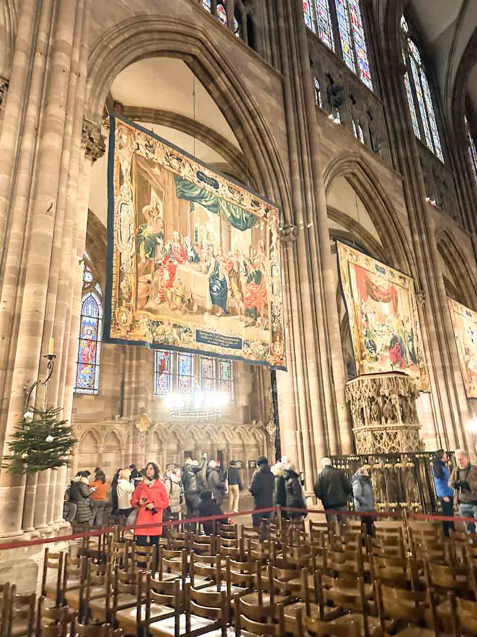 Visitors admiring the grand tapestries hanging within the nave of Strasbourg Cathedral