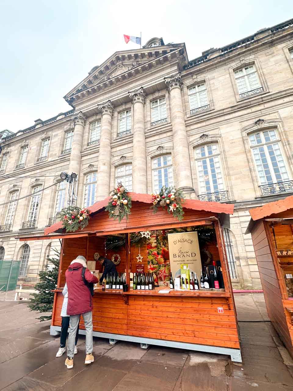 A chalet-style stall in front of the grand Palais Rohan in Strasbourg, offering a selection of Alsace wines