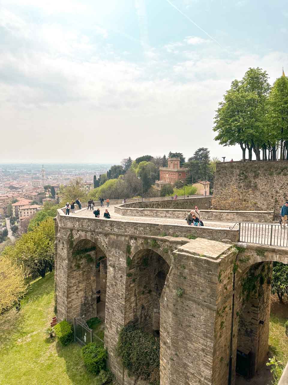 A stone viaduct overlooking a panoramic view of Bergamo's lower cityscape