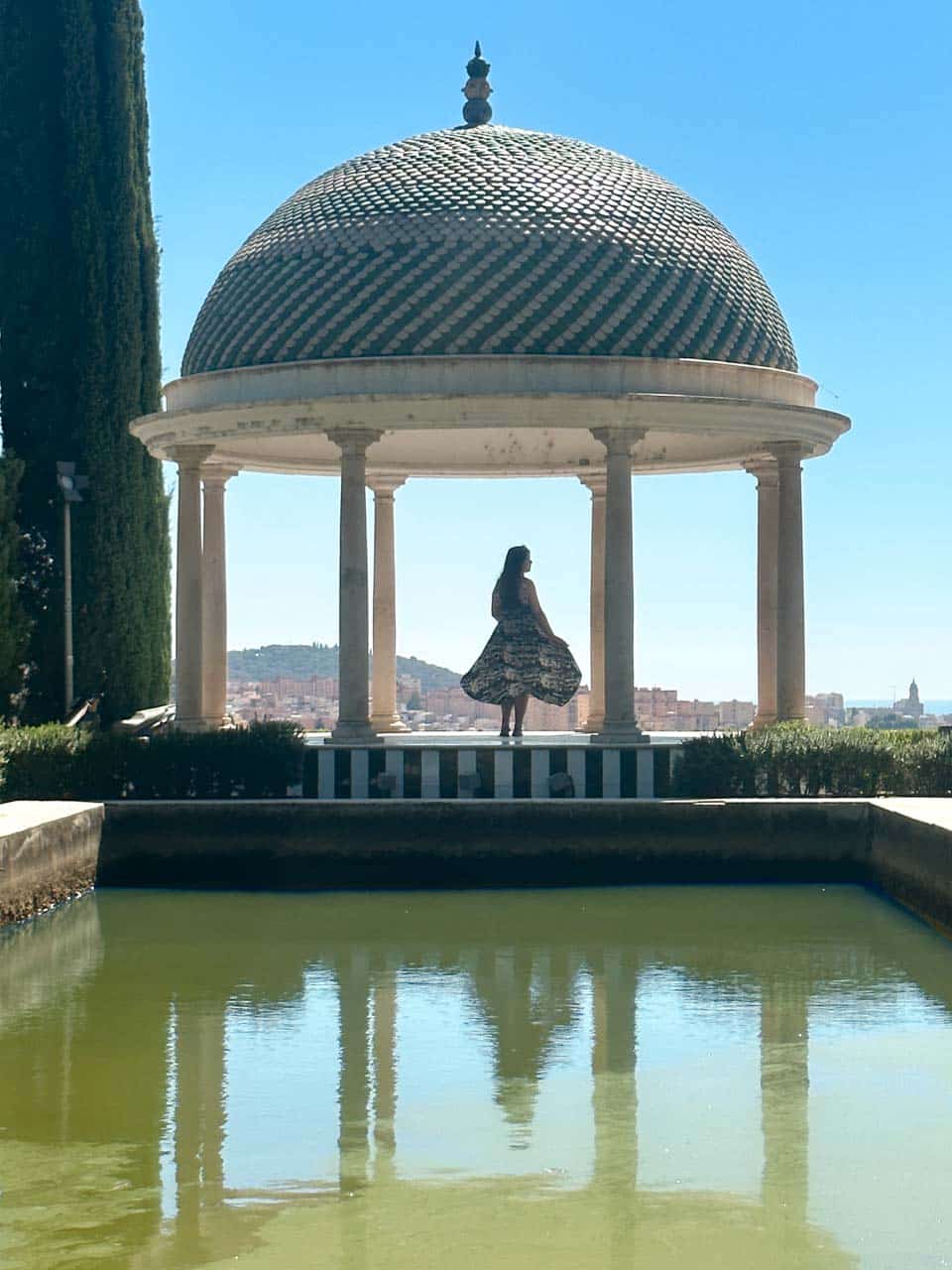 A woman in a dress standing under a patterned dome in the La Concepci&oacute;n Historical Botanical Garden in Malaga, with a pond in the foreground