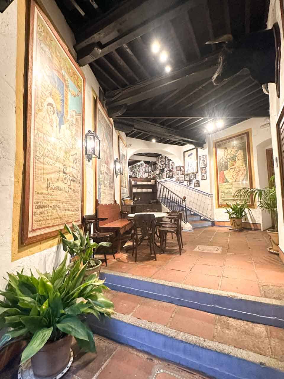 The interior of Bodega El Pimpi in Malaga, Spain, with a tiled walkway, historic posters on the walls, and a traditional wooden ceiling
