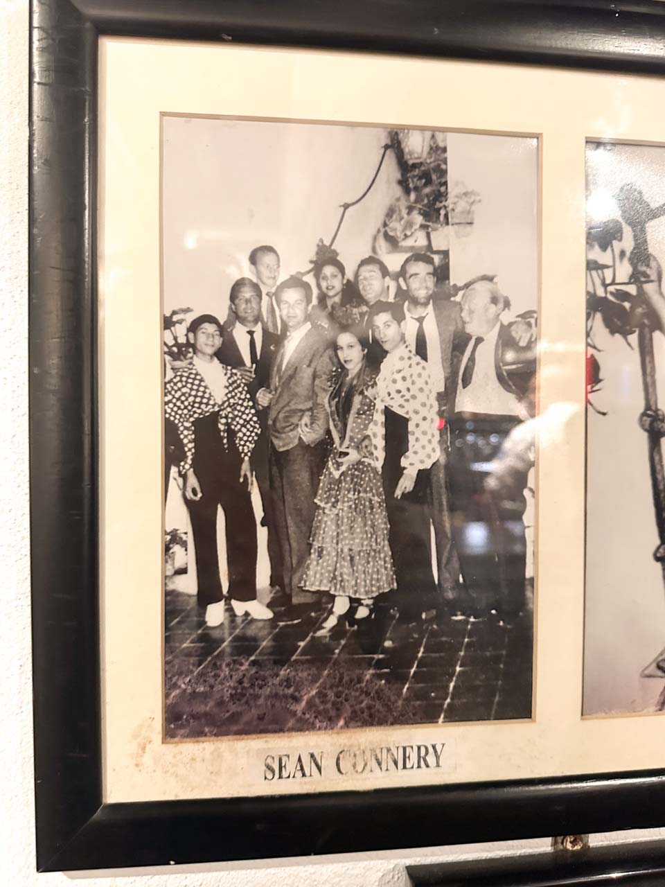 A framed black and white photo of a group including Sean Connery, displayed on a wall among other pictures at Bodega El Pimpi in Malaga, Spain