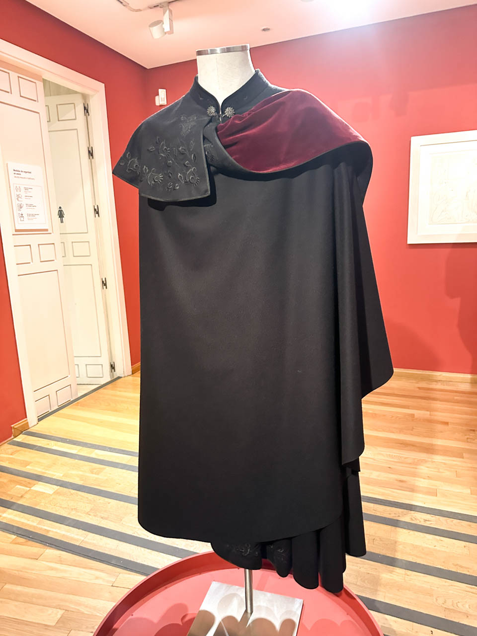 A traditional Spanish cape or "capote de paseo" displayed on a mannequin against a vivid red background inside the Museo Casa Natal de Picasso in Malaga, Spain