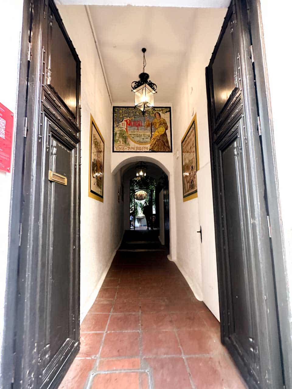 Narrow passageway with vintage posters on the walls, leading to the courtyard of Bodega El Pimpi in Malaga