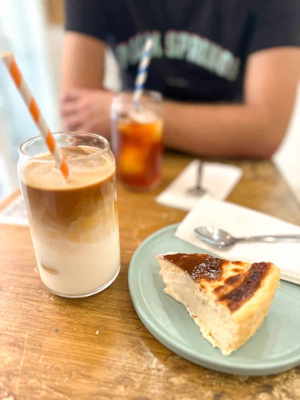 A glass of iced coffee with milk and a slice of cheesecake on a blue plate in a caf&eacute; in Malaga