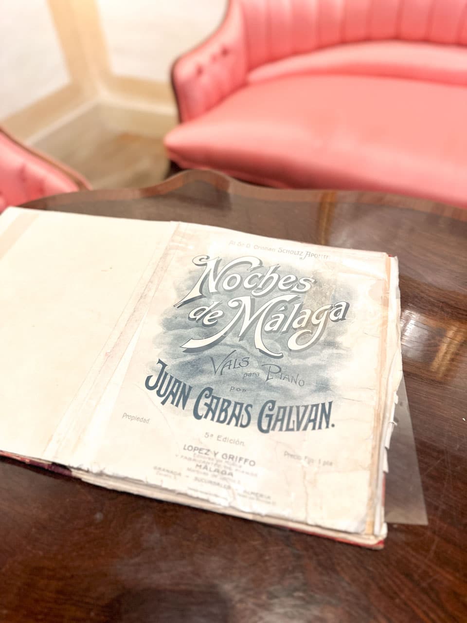 A vintage music sheet for &lsquo;Noches de Malaga&rsquo; resting on a wooden table in front of a plush pink sofa