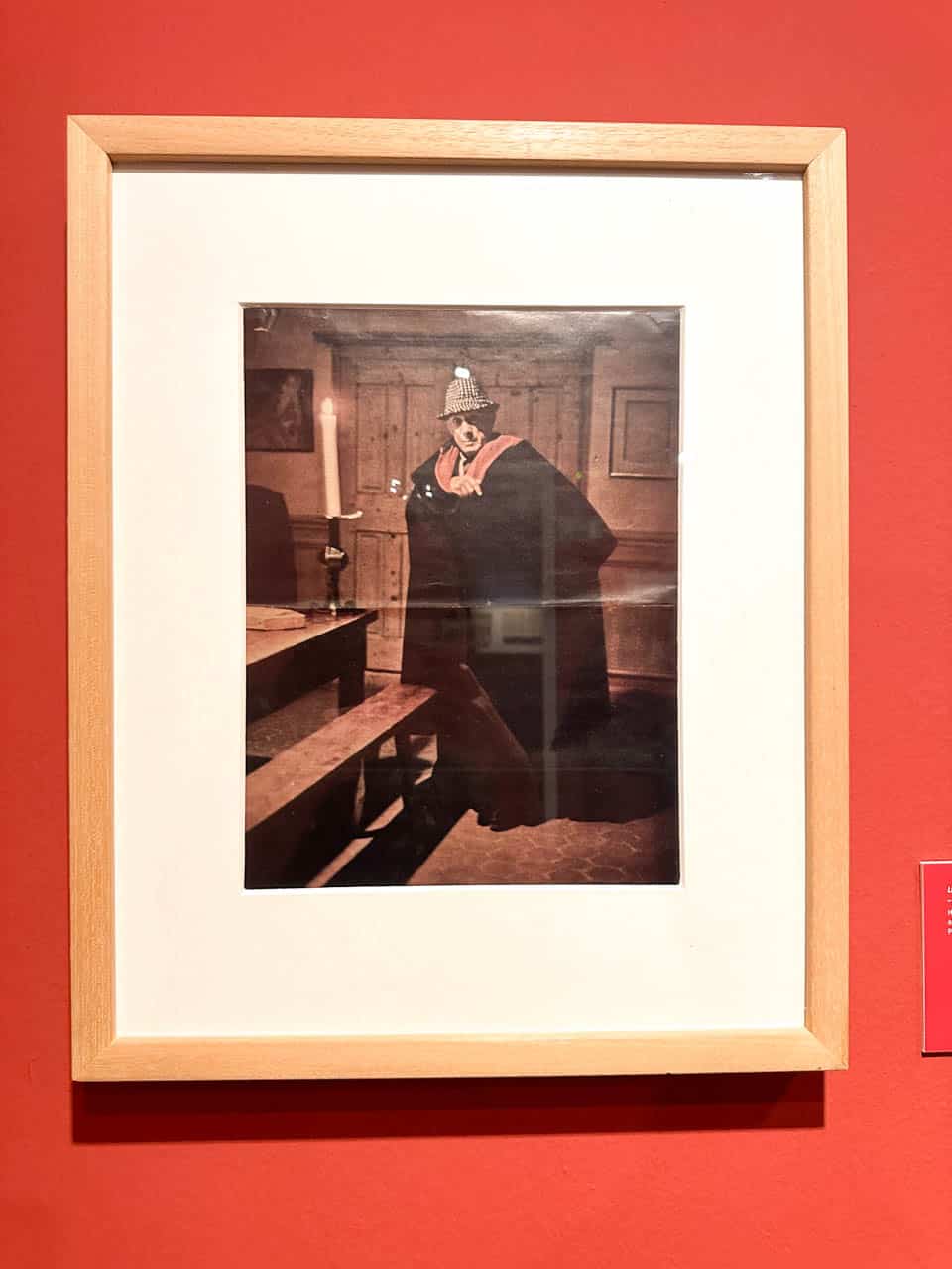 A framed photo on a red wall showcasing Pablo Picasso in a traditional Spanish cape