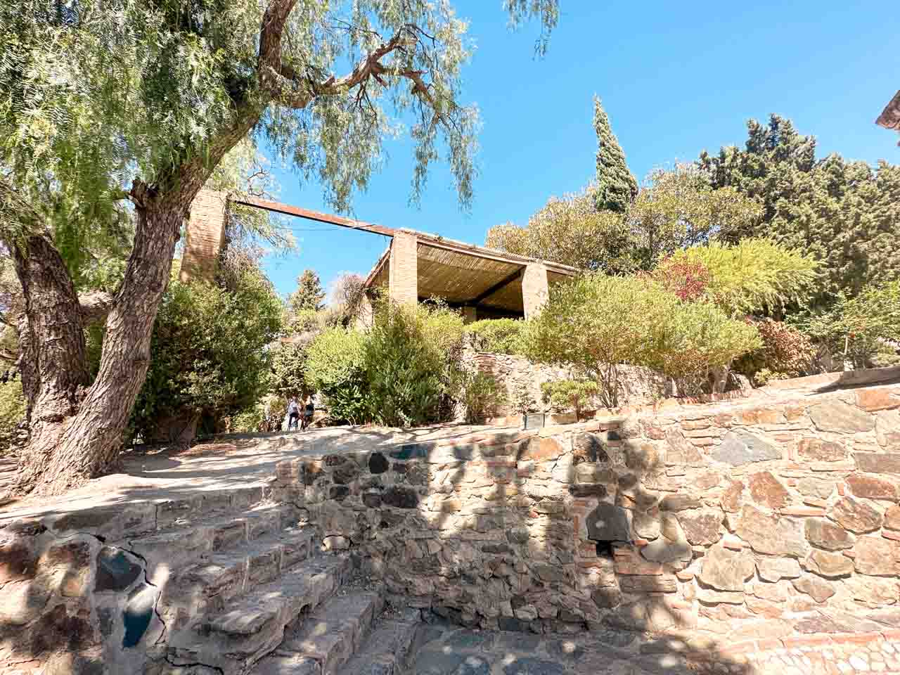 A leafy path leading to a wooden gazebo inside the Gibralfaro Castle grounds in Malaga, Spain