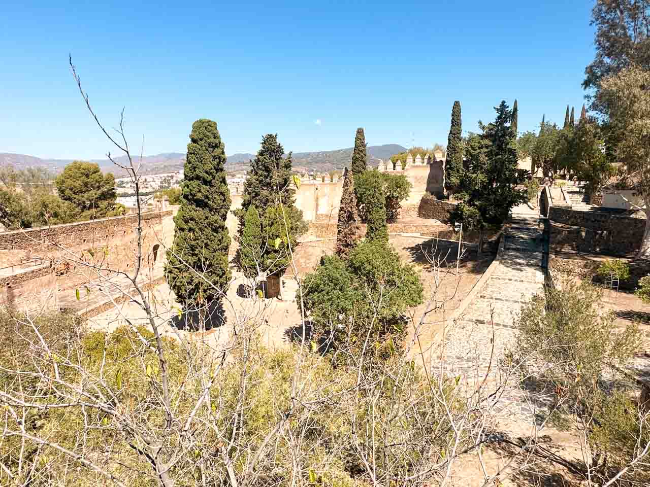 A panoramic view over the walls and towers of Gibralfaro Castle, surrounded by cypress trees