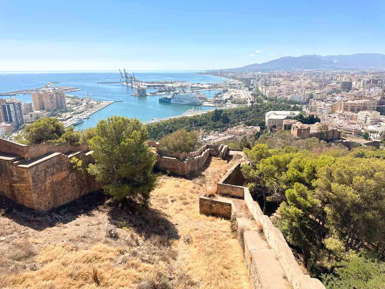 The panorama from Gibralfaro Castle, featuring the port of Malaga with its ships and the cityscape, set against the Mediterranean Sea
