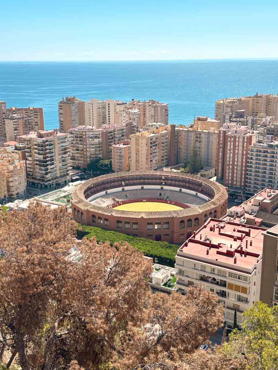 An aerial view of Malaga&rsquo;s bullring surrounded by blocks of flats, with the Mediterranean Sea stretching into the horizon
