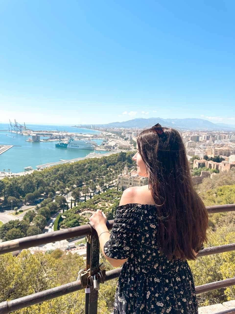 A woman with long dark hair admiring the view of Malaga&rsquo;s city and sea from a spot on the way up to Gibralfaro Castle