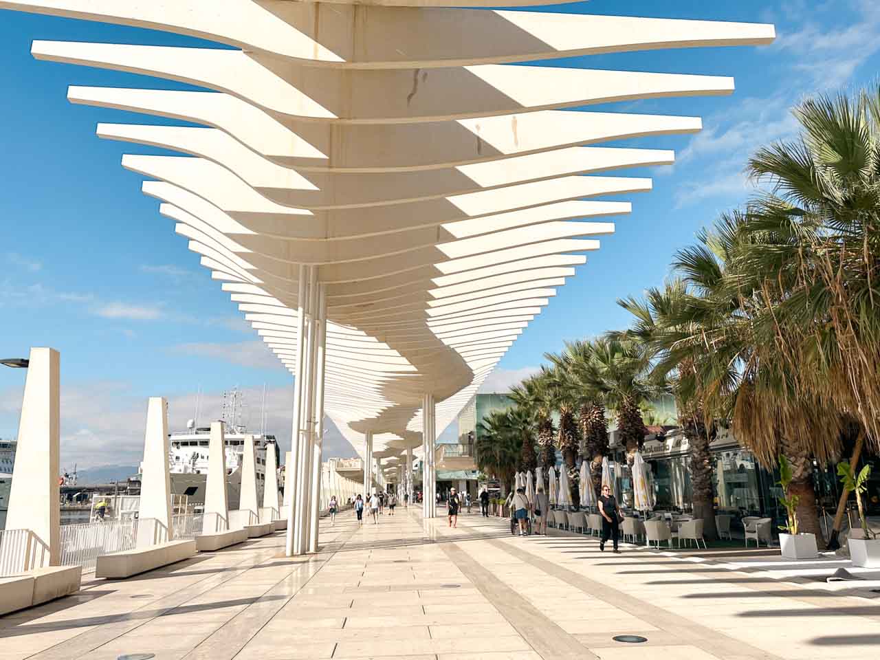 A modern, white wave-like structure on the Muelle Uno promenade in Malaga, Spain